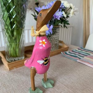 wooden painted duck on a table, the duck has been panited pink and yellow
